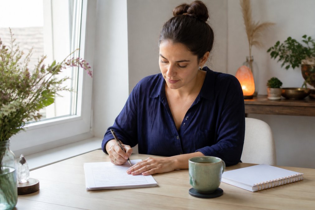 Eine Frau sitzt konzentriert am Laptop und füllt das Bestellformular für ihr Mond-Abo aus, mit einer Tasse Tee und einem Notizbuch auf dem hellen Schreibtisch