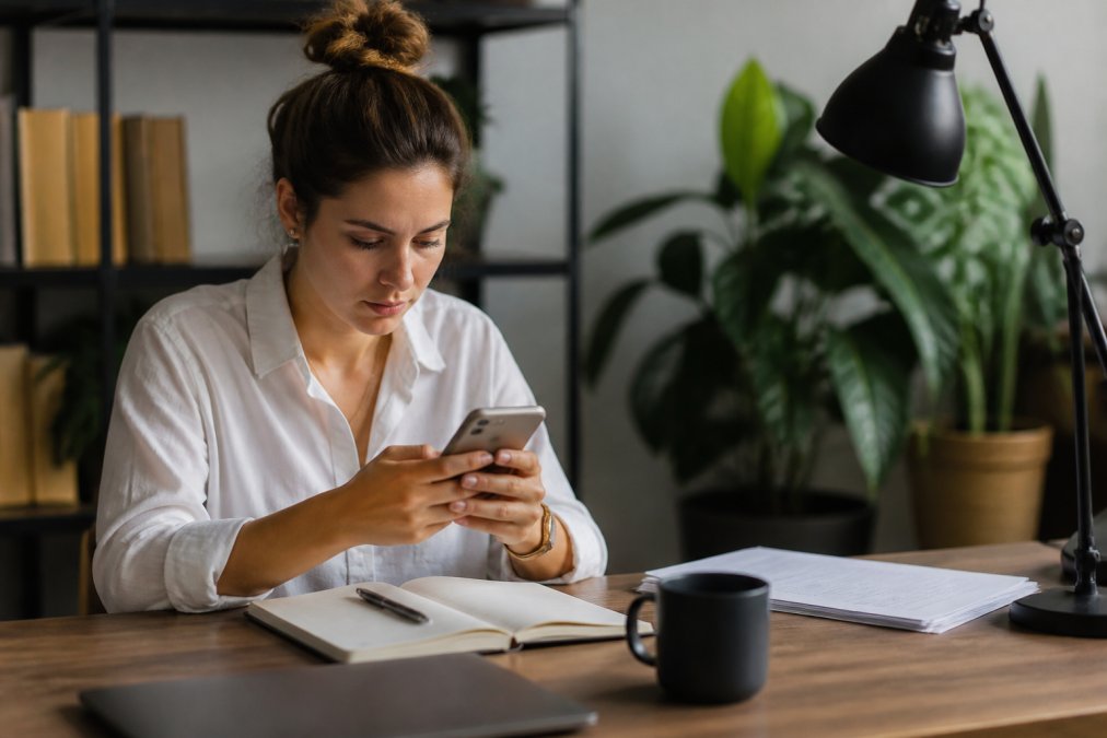 A busy professional at a desk quickly reviewing content on their phone during a work break, showing a simple, time-efficient workflow