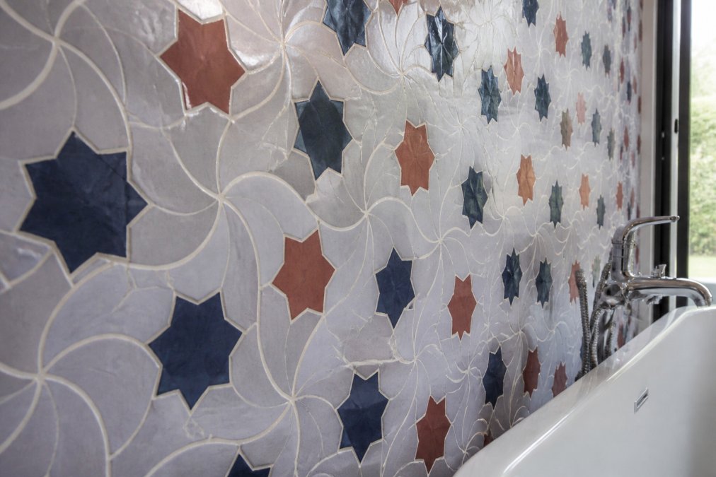 Close-up of intricate zellige mosaic tile work on a bathroom wall, showing geometric patterns in blue, white, and terracotta tones with natural light highlighting the handcrafted precision and dimensional depth
