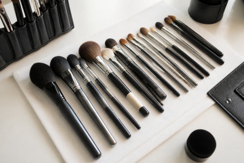 Close-up of an organised collection of professional makeup brushes in various sizes and shapes, arranged neatly on a white surface with natural lighting, displaying bristle texture and handle detail