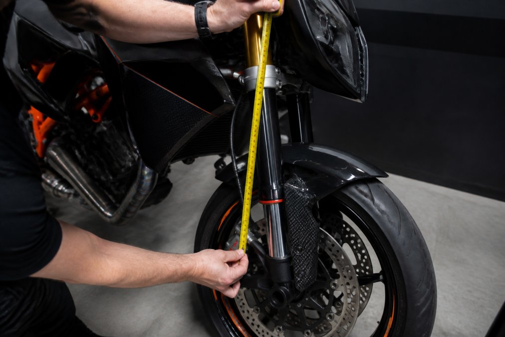 Motorrijder die sag meet aan de voorvork met een meetlint, waarbij de meetpunten duidelijk zichtbaar zijn tegen het frame van de motor