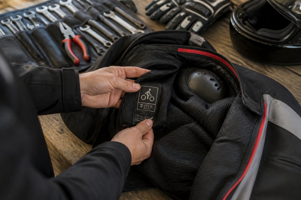Rider examining the CE safety rating label stitched inside a motorcycle jacket with shoulder armor visible