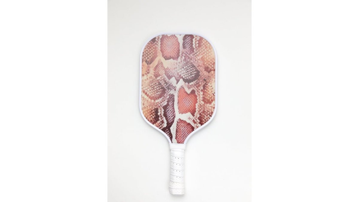 Close-up of five pickleball paddles displayed together, showing the Miami, Monaco, Paris, Ibiza, and Mozambique Lulla Sport designs with their distinct color patterns and carbon fiber faces visible, arranged on a dark surface with natural side lighting