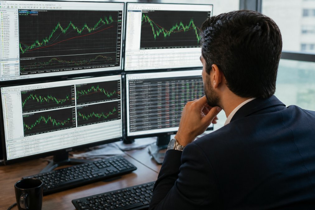 Professional trader at desk with multiple monitors displaying MT5 trading platform with real-time forex charts, candlestick patterns, and live order execution interface showing multiple currency pairs
