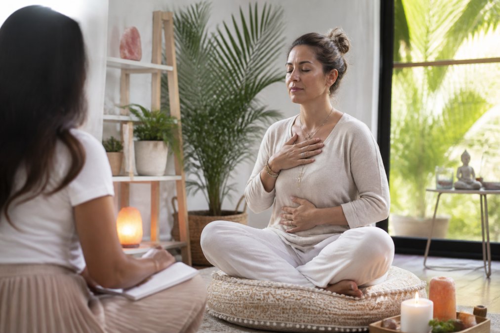 A woman practicing multidimensional energy healing while meditating on a cushion surrounded by crystals and a candle.