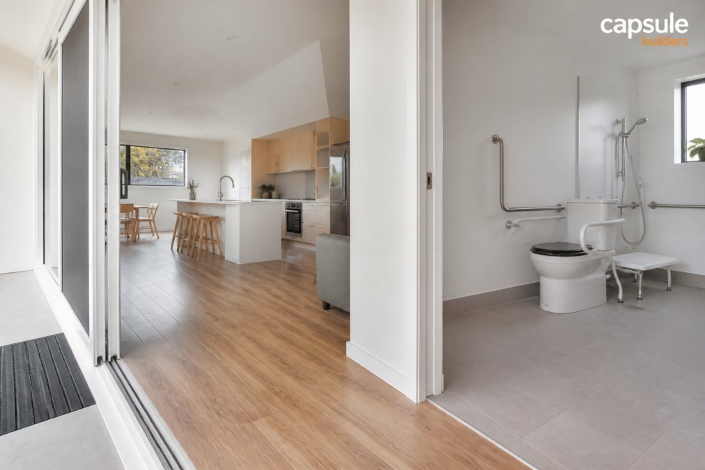 Interior of a bright, open-plan modular home with wide doorways, a step-free entrance, and grab rails in a modern bathroom, showing accessible design features suited to an older resident