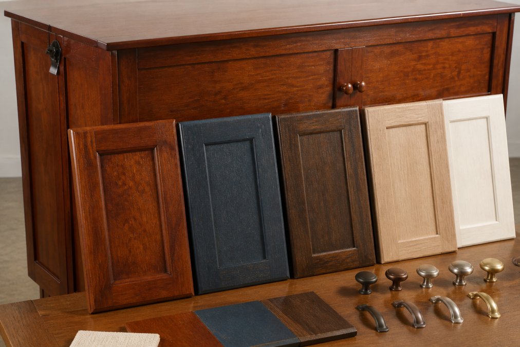 Close-up detail of various wood finishes and cabinet hardware options showing texture, grain, and color variations including Harvest Brown, Antique Blue, and natural wood tones