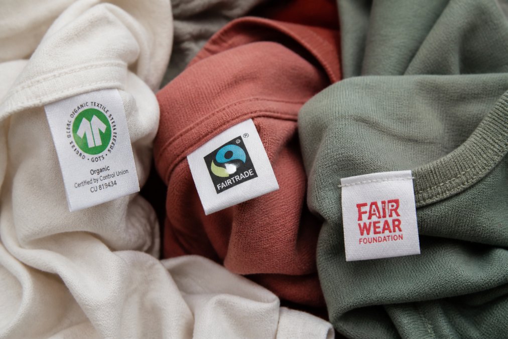 Nahaufnahme von Zertifizierungssiegeln und Etiketten auf nachhaltiger Kleidung - GOTS, Fairtrade, Fair Wear Foundation Logos sind deutlich sichtbar