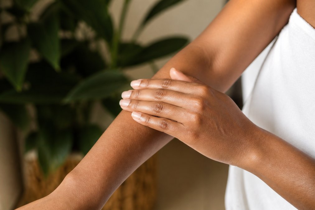 Close-up of hands applying natural body oil to dry skin on arm with warm natural lighting, showing non-greasy absorption and healthy skin tone