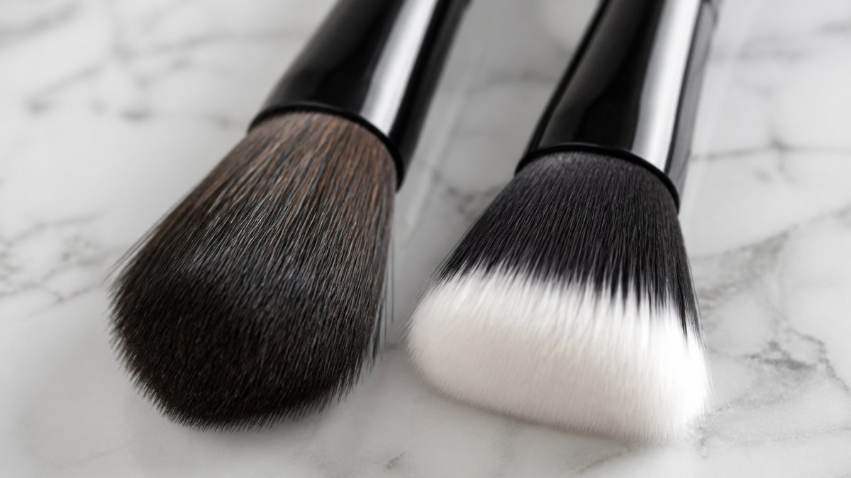 Close-up of two makeup brushes side by side on a clean marble surface, one with natural bristles and one with synthetic fibers, soft natural lighting