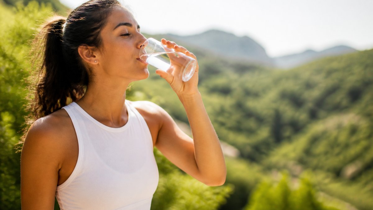 Person drinking water from a glass outdoors in natural sunlight, looking refreshed and alert