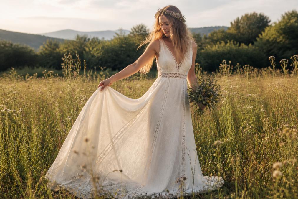 A bride wearing a flowing bohemian wedding dress made of natural linen and cotton, standing in a sunlit meadow with wildflowers, soft natural lighting, relaxed and ethereal atmosphere