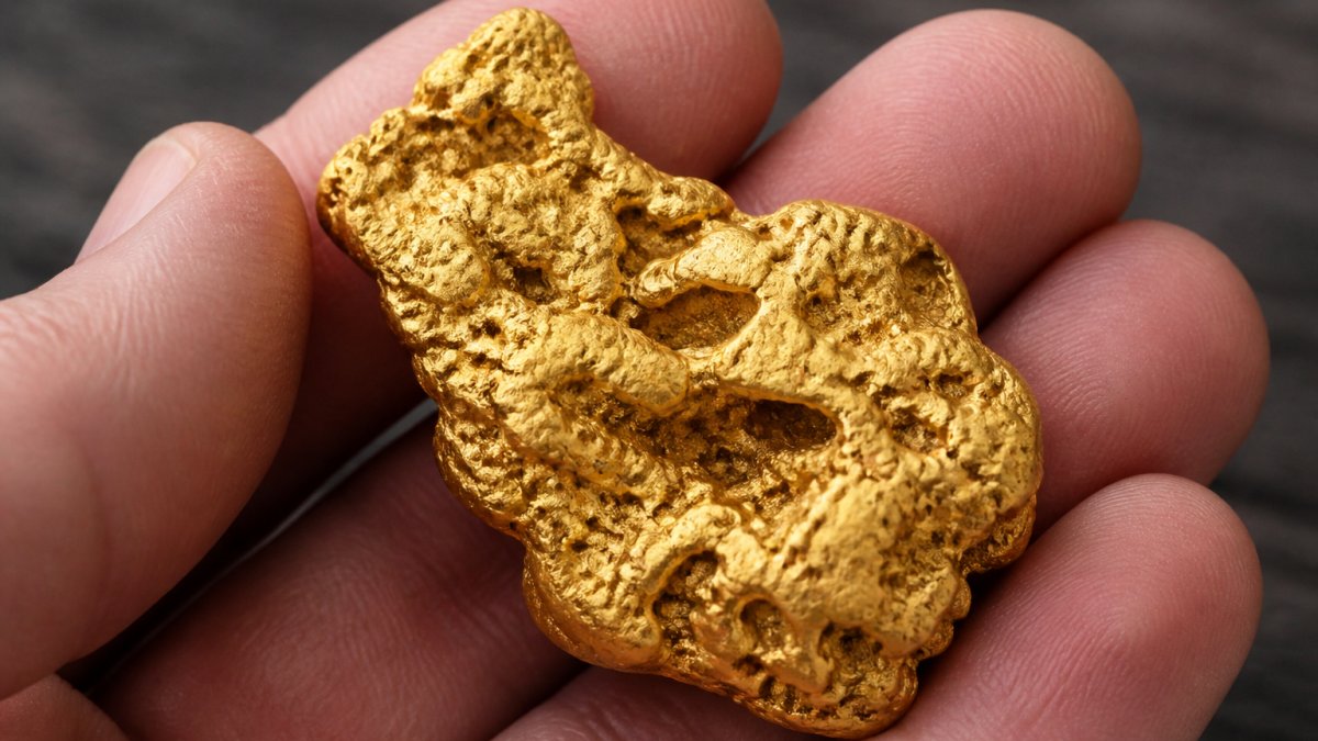 Close-up of a natural Australian gold nugget held in hands, showing textured surface with natural golden lustre, irregular organic shape, and visible surface cavities against a neutral background