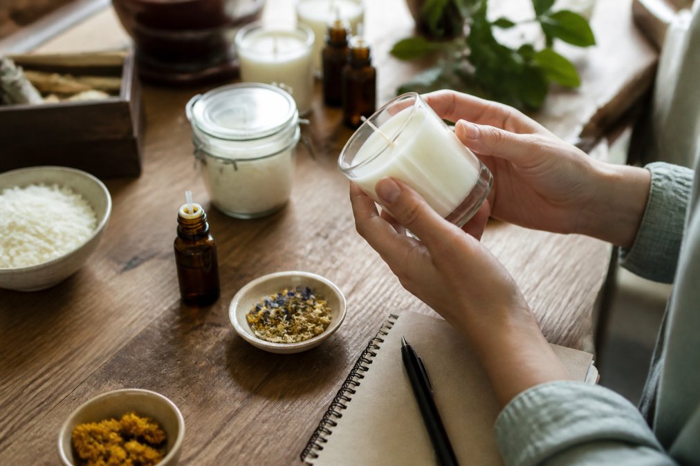 Close-up of hands holding a scented candle jar, examining the label for ingredient information and certifications in natural lighting