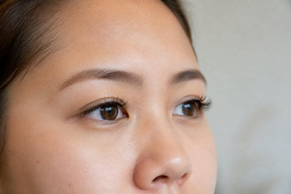 Close-up of a woman with natural-looking eyelash extensions, soft lighting, neutral background, showing defined but weightless lashes