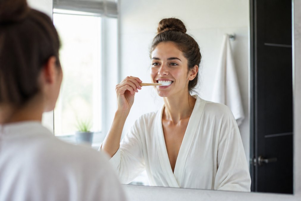 Person carefully brushing teeth with natural toothpaste product showing proper technique and healthy gum appearance in morning bathroom setting with soft natural lighting