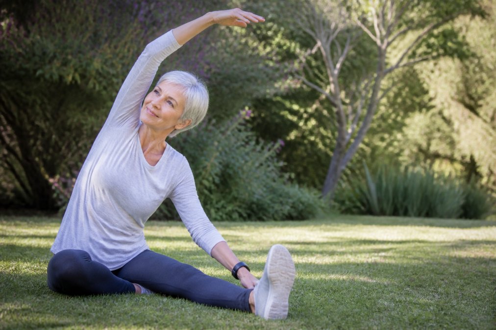 Active senior performing gentle stretching exercise outdoors in natural daylight, demonstrating proper form with relaxed posture and peaceful expression