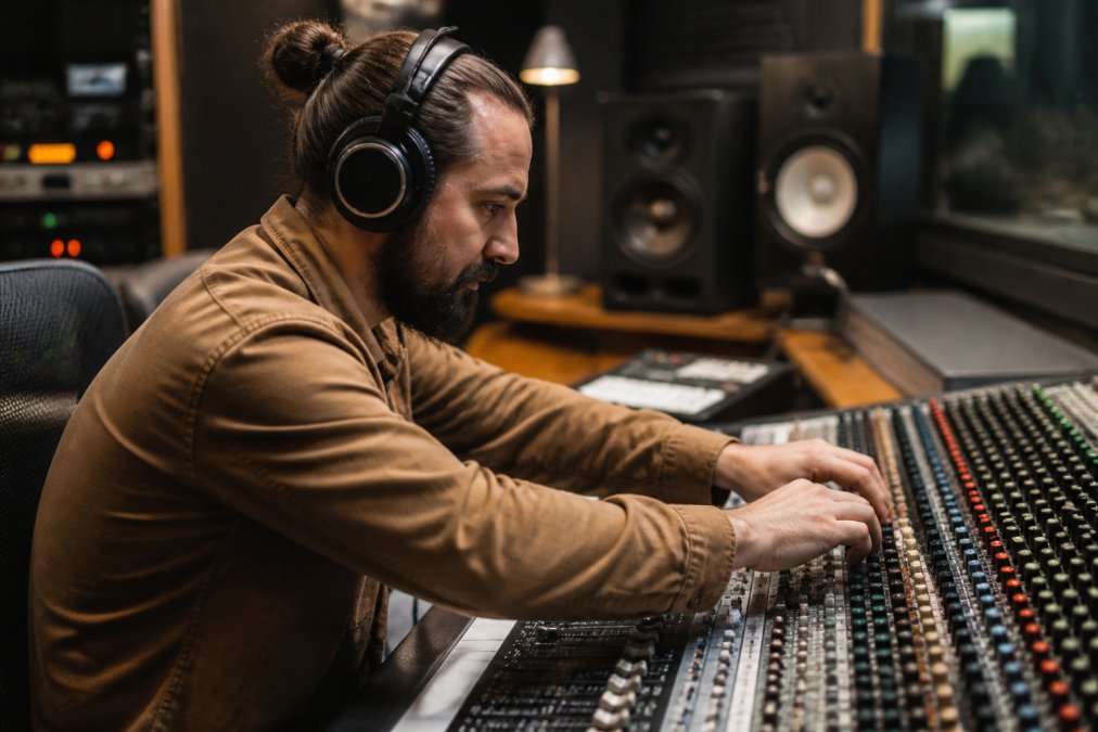 Sound engineer adjusting levels on a mixing console to produce a natural sounding ai voice in a recording studio.