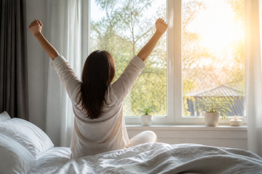 Person waking up feeling refreshed as morning sunlight streams through bedroom windows to improve sleep quality