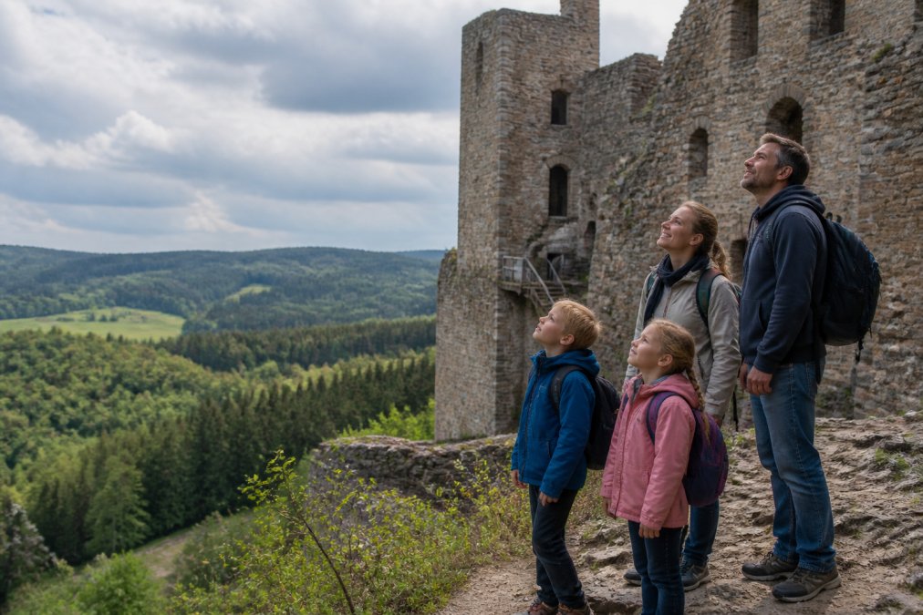 Eine Familie mit zwei Kindern steht vor einer mittelalterlichen Burgruine im Waldviertel, die Kinder schauen begeistert nach oben, die Eltern lächeln, im Hintergrund grüne Hügel und Wald