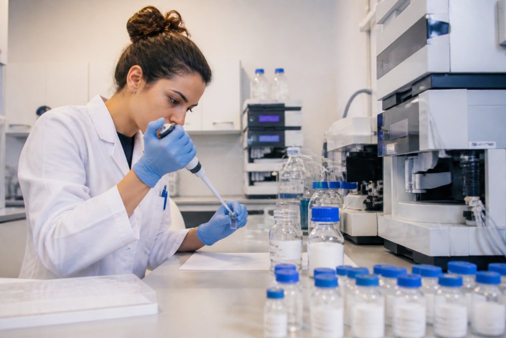Laboratoriumtechnicus die voorzichtig pipetteert in precisie-testapparatuur in een schoon onderzoekslaboratorium, met geëtiketteerde peptide-flessen en chromatografische instrumenten op het werkblad