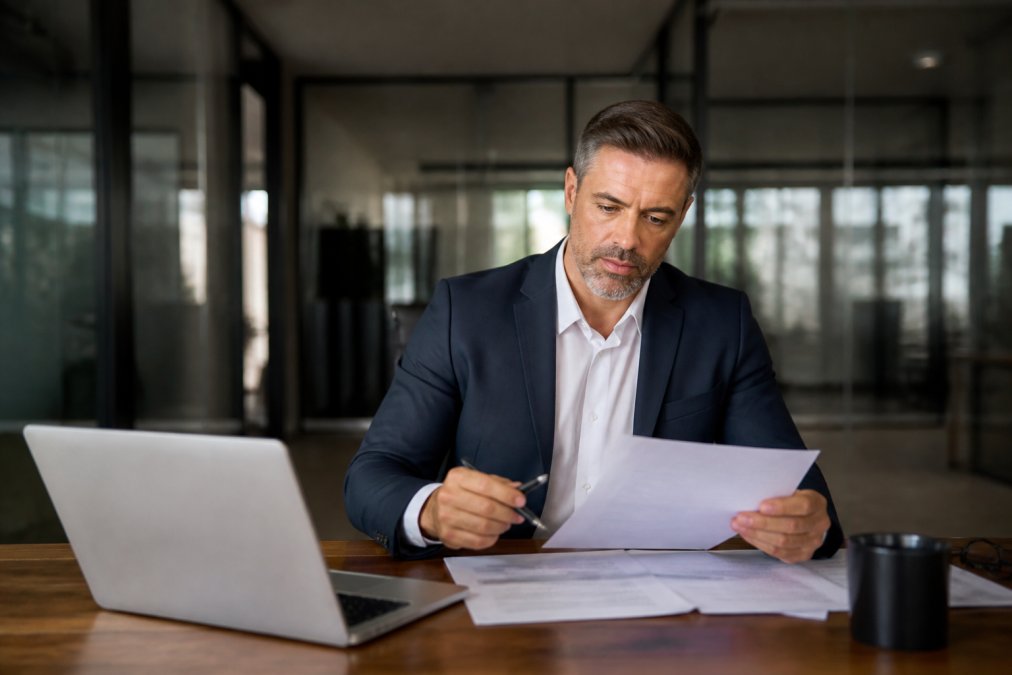 Financial advisor reviewing retention bonus offer documents at a modern office desk with a laptop and coffee