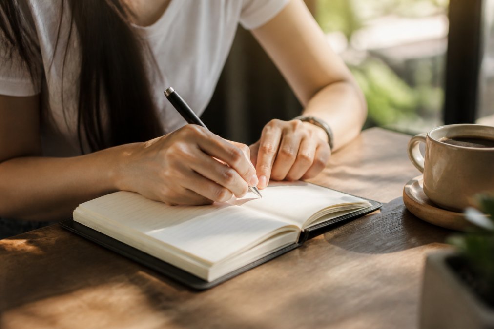 Person writing in a journal with a coffee cup, practicing law of attraction techniques on a wooden desk.