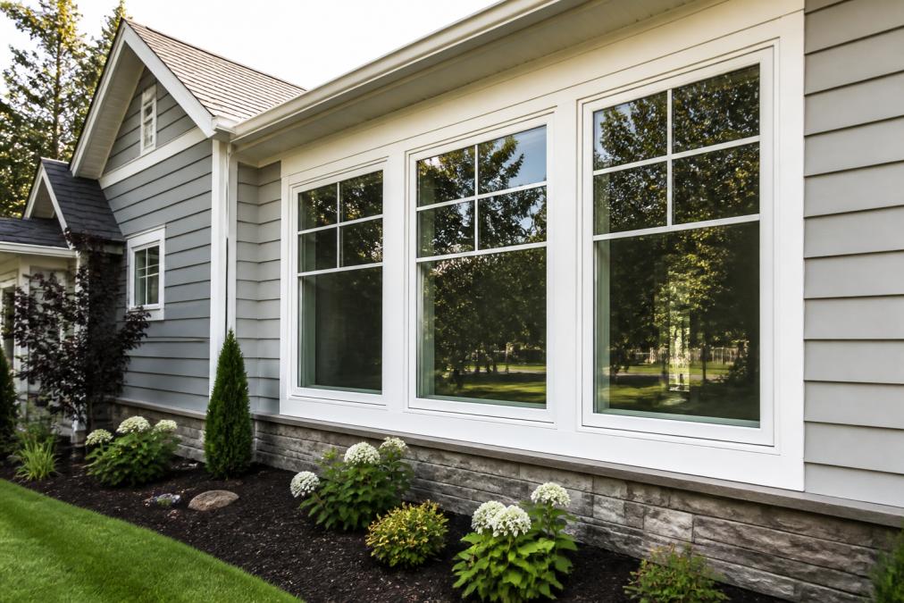 Home exterior featuring newly installed modern windows with clean bright frames, natural sunlight streaming through glass panes, manicured landscaping and fresh siding visible in background