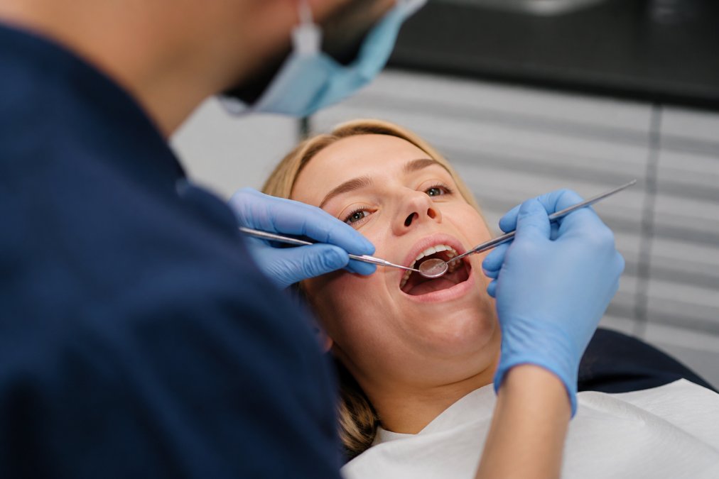 Close-up of a patient's mouth during a dental examination, showing a dentist's hands and instruments near the teeth area, with natural clinical lighting