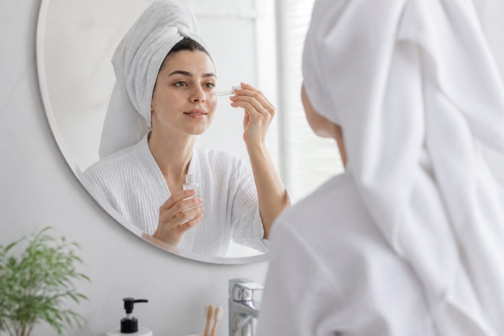A woman with sensitive skin gently applying a niacinamide serum in front of a mirror in a bright bathroom for maximum benefits.