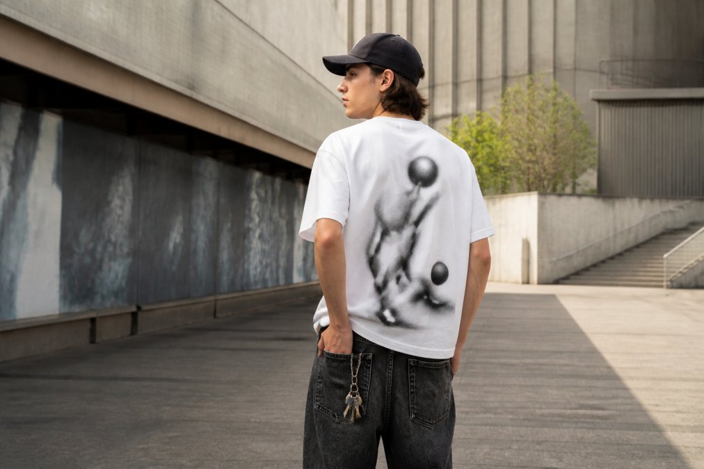 Jonge persoon gekleed in niche streetwear met opvallend backprint t-shirt, zelfbewust poseren in urban setting met natuurlijke verlichting, styling met onafhankelijke merkstukken die persoonlijkheid uitdrukken
