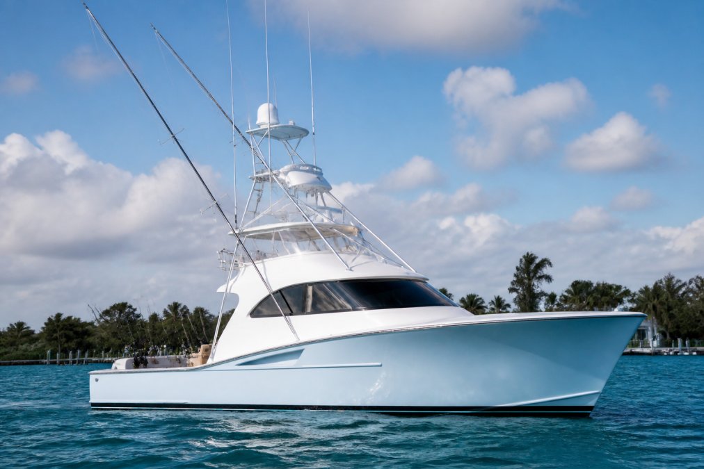 High-end sport-fishing yacht anchored offshore with fishing equipment visible on the hardtop and deck, showing the vessel's distinctive hull design and cabin structure in natural daylight with blue water