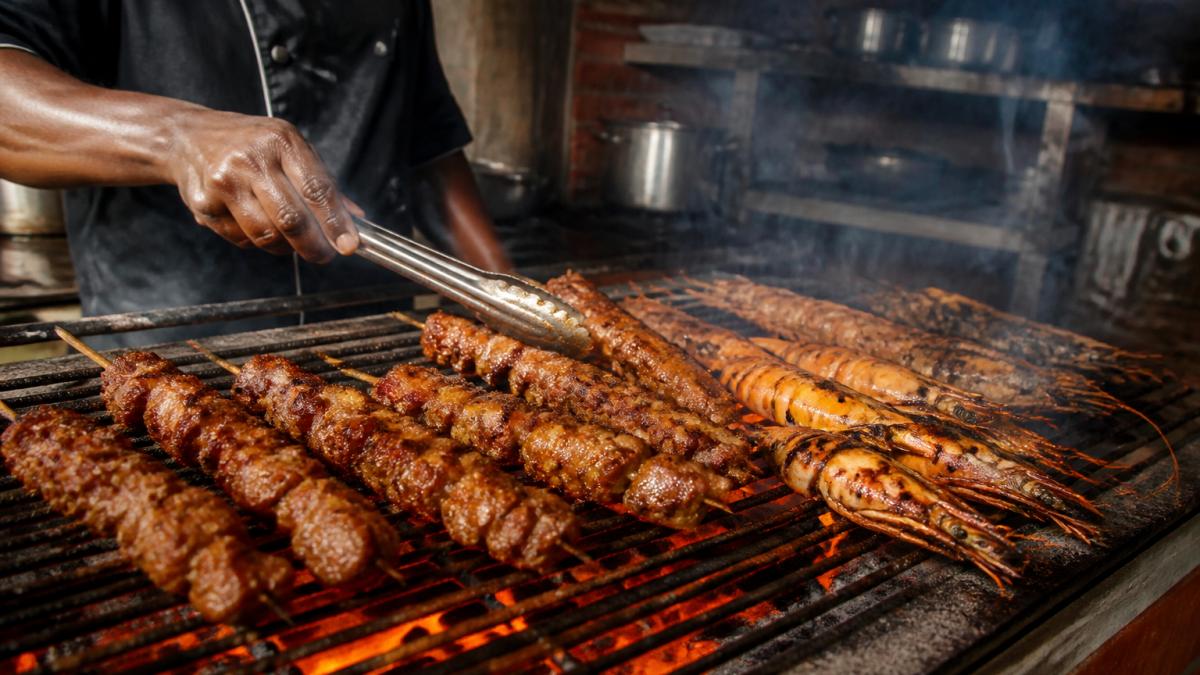 Close-up of marinated meat skewers and whole prawns charring over glowing coals on a restaurant grill, a chef's hands turning them with tongs, warm amber light and a dim open kitchen behind