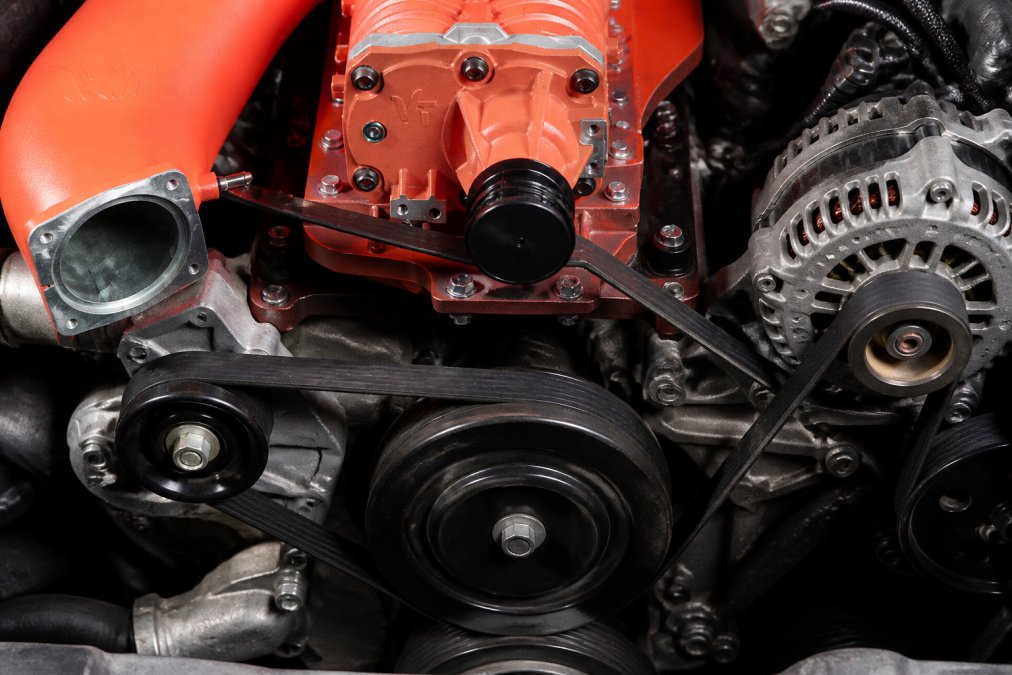 Close-up of serpentine belt routing around crankshaft pulley, supercharger pulley, and alternator pulley on a Nissan Frontier engine, showing proper alignment and tension points
