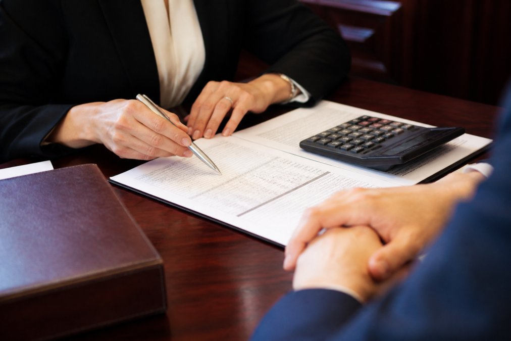 Close-up of hands holding pen and reviewing legal document with calculator and cost breakdown sheet on mahogany desk in professional office setting