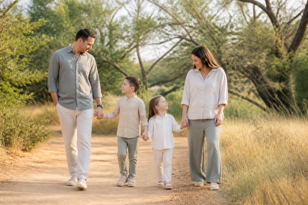 Family of four wearing coordinated earth-tone button-down tops and relaxed-fit pants in cream and warm gray tones during outdoor photo session in natural sunlight, showing subtle coordination that feels intentional rather than forced