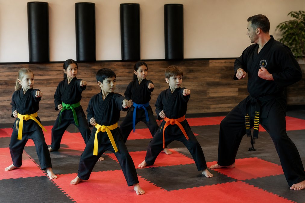 Instructor teaching basic stances to non-competitive martial arts kids in a bright, welcoming studio.