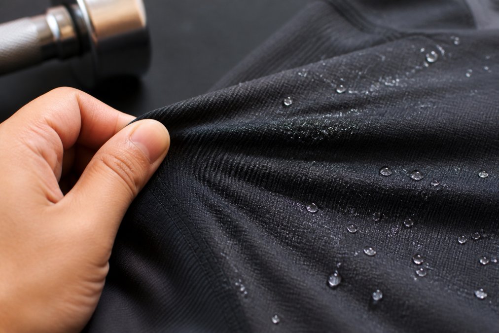 Close-up of high-quality synthetic athletic fabric with visible four-way stretch construction, moisture beading on surface under bright studio lighting