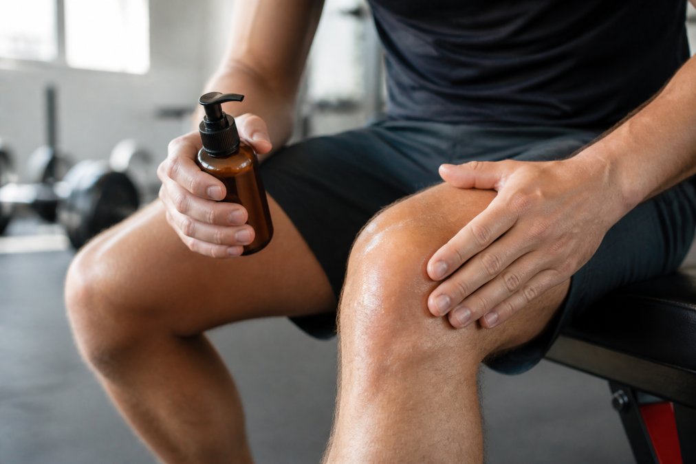 Athlete's hands holding non-greasy CBD lotion bottle, demonstrating proper application technique on knee joint with clear product absorption visible