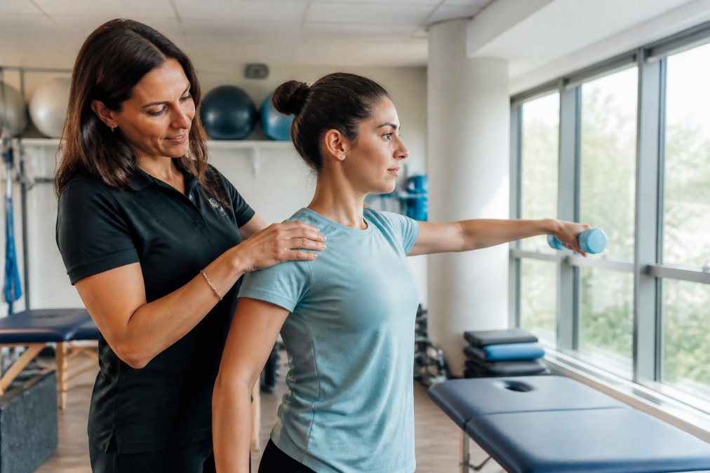 Physical therapist working with patient performing shoulder range of motion exercise in modern clinical setting with natural lighting