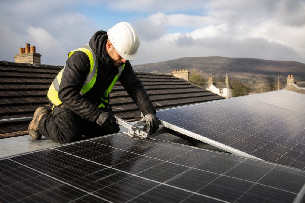 Professional solar installer adjusting mounting brackets on north-facing roof panels with visible tilt angle measurement tool, afternoon Scottish light