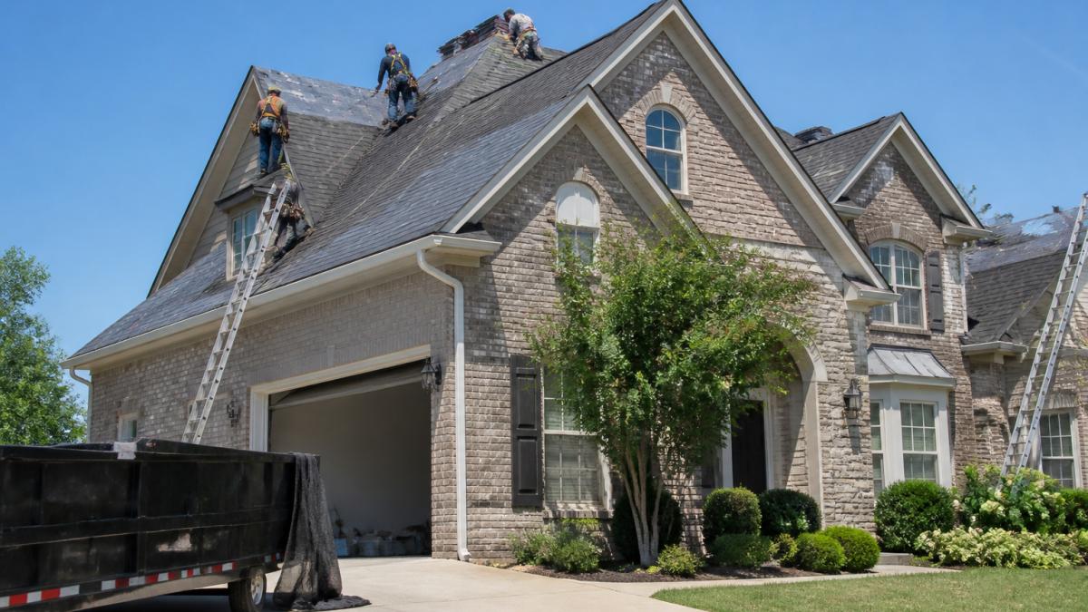 Roofing crew in safety harnesses installing shingles during a roof replacement project on a sunny day