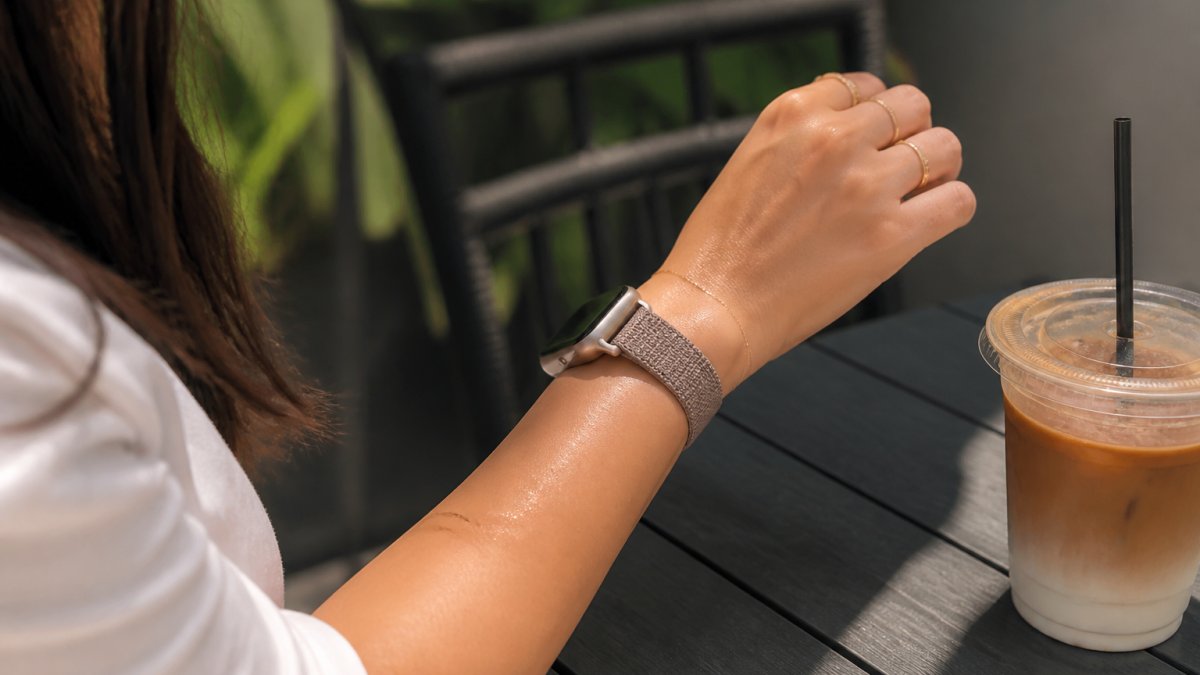 Woman wearing a woven fabric watch band on her wrist while relaxing outdoors with a cool drink nearby