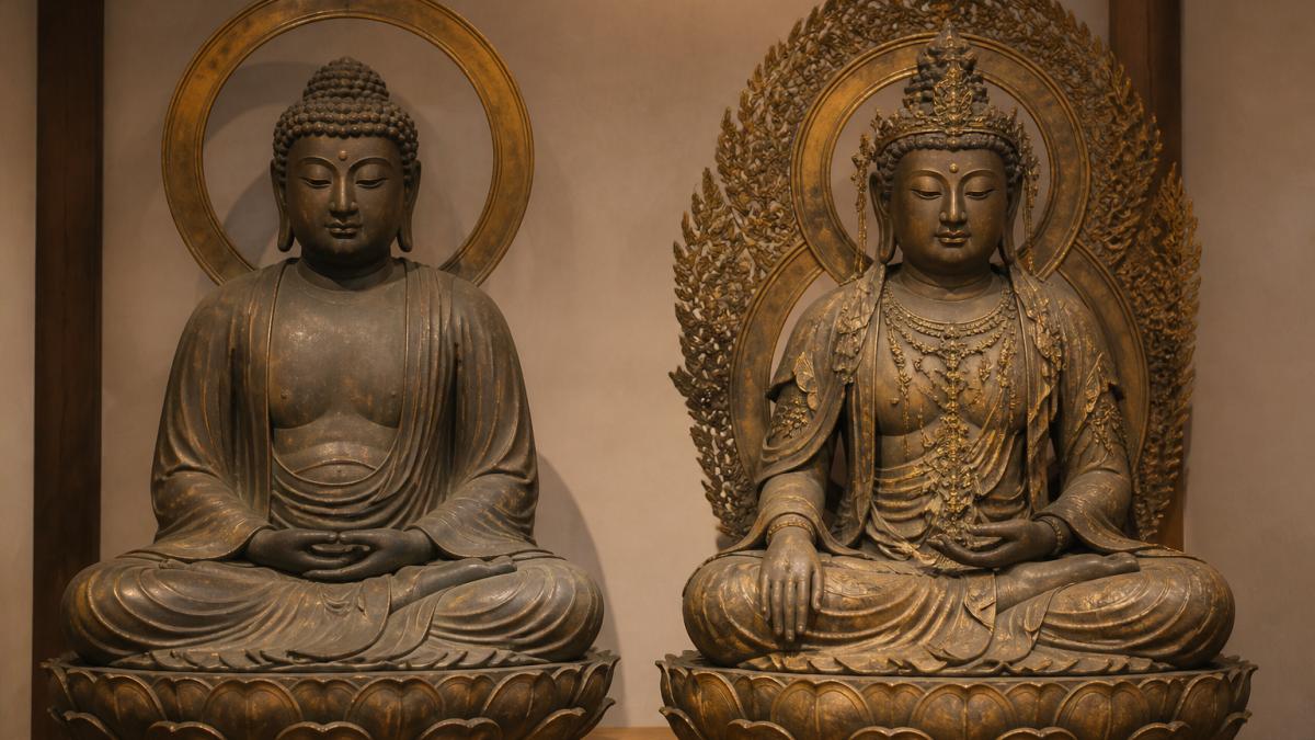Two Japanese Buddhist statues displayed side by side in a gallery: one in plain monastic robes with a simple halo, the other wearing a jeweled crown and ornate necklace, lit warmly to show the contrast in drapery and adornment