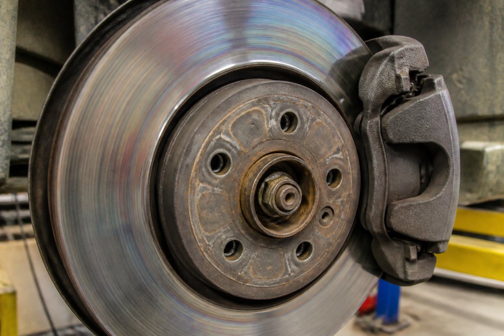 Close-up of Porsche brake rotor surface showing thermal discoloration patterns and brake pad contact area with caliper assembly visible in workshop lighting