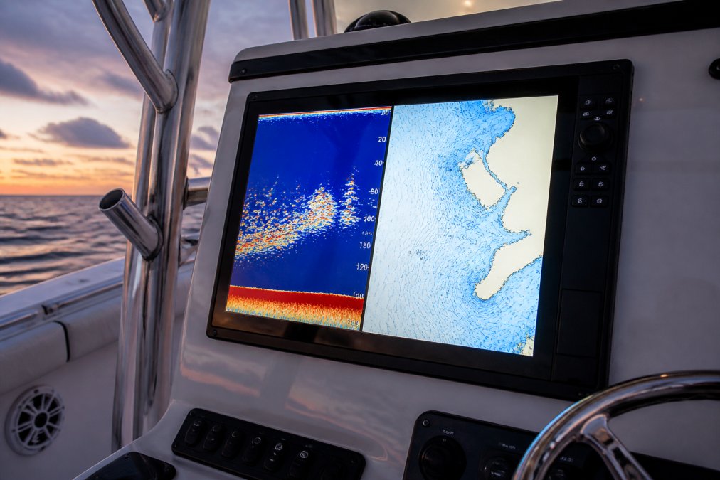 Close-up of a multifunction display mounted on an offshore fishing boat console at dusk, showing a split-screen sonar view with fish targets and a chartplotter with depth contours visible