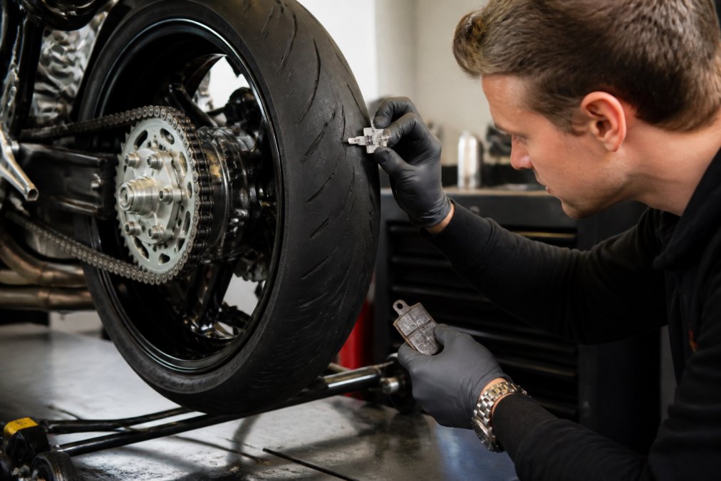 Technicus die bandenprofiel meet met profielmeters en remblokken inspecteert op slijtage aan tweedehands motorfiets in professionele werkplaats