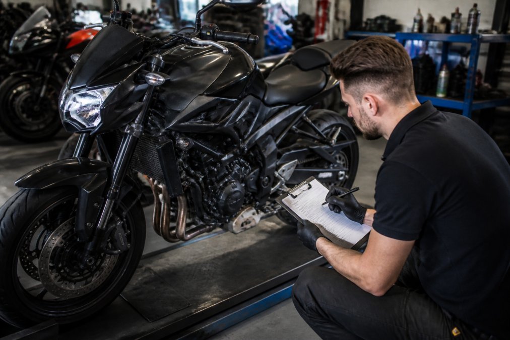 Technicus voert gedetailleerde inspectie uit op motorfiets in werkplaats, controleert motorcomponenten en maakt aantekeningen op inspectieformulier
