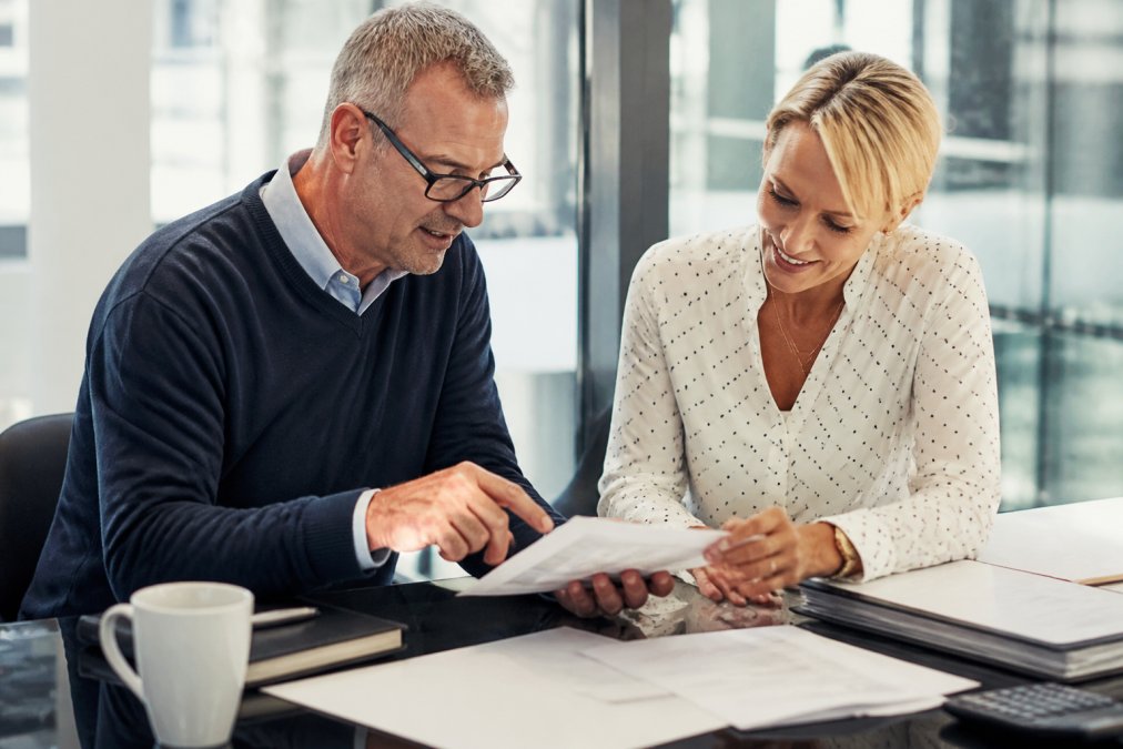 Benefits consultant meeting with business owner at a desk, reviewing insurance documents and coverage options together in a professional office with natural lighting