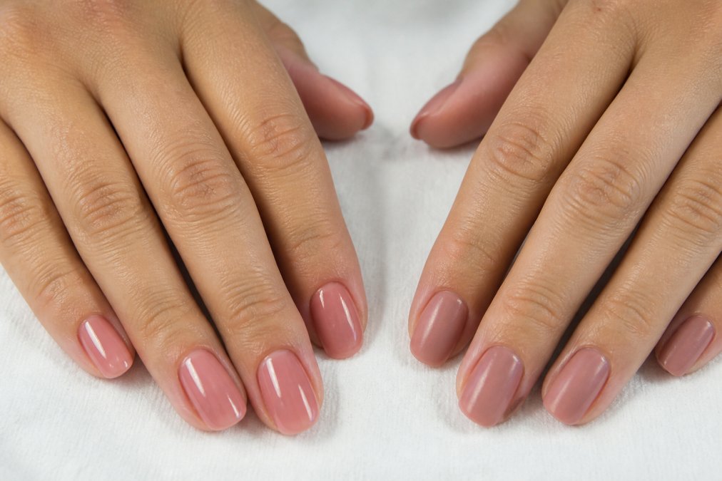 Gros plan de deux mains côte à côte sur une surface blanche, l'une avec une manucure gel brillante et l'autre avec un vernis classique, montrant la différence visuelle de brillance et de texture sous un éclairage naturel doux